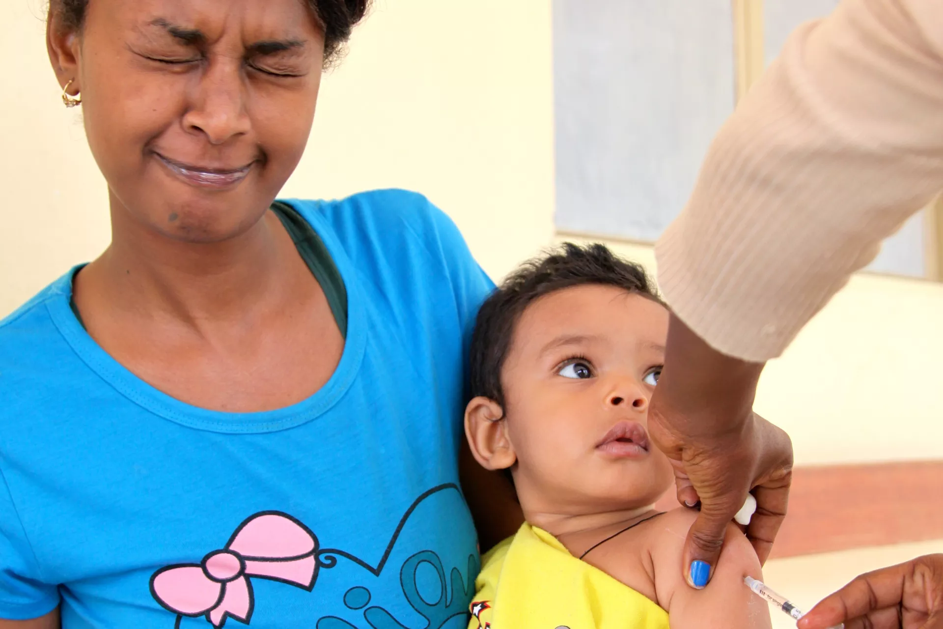 Uma mulher faz careta quando um profissional de sa&uacute;de vacina seu filho contra o sarampo na Eritreia 