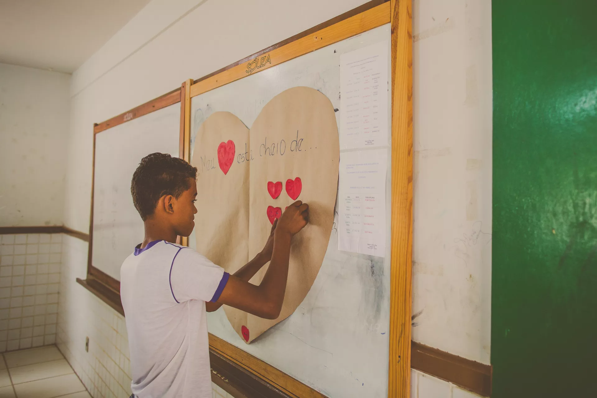 um adolescente prega um cora&ccedil;&atilde;o no quadro de sua sala de aula