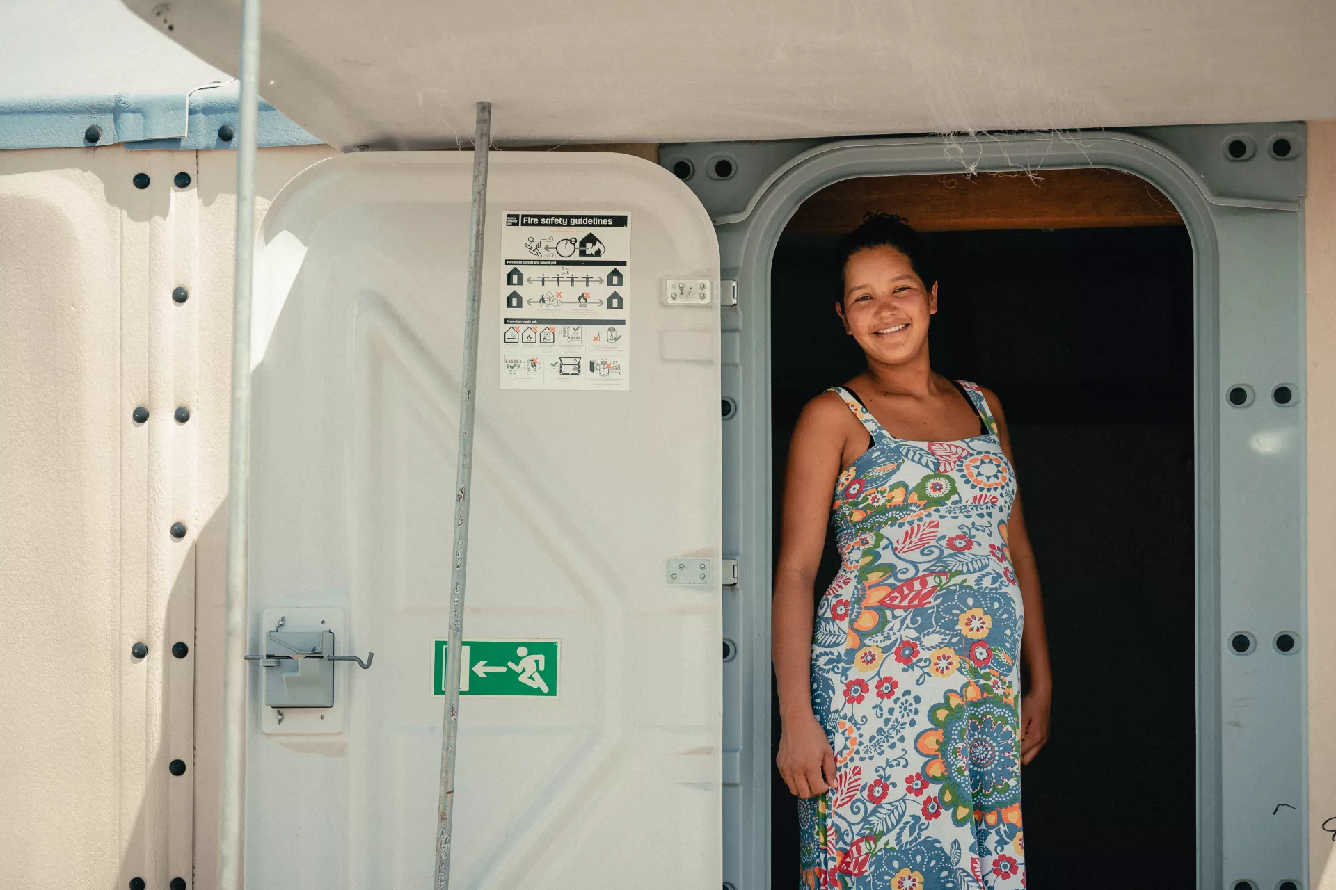 Foto mostra uma mulher jovem gr&aacute;vida para na porta de um trailer.
