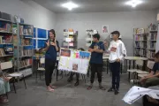jovens apresentam trabalho segurando cartolina em biblioteca