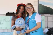 funcion&aacute;ria do Unicef e jovem ind&iacute;gena seguram boneco de pel&uacute;cia azul, o Unicefito