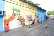 Foto mostra um muro grande sendo grafitado por alguns adolescentes e jovens.