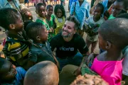 o ator Bruno Gagliasso, usando a camiseta do UNICEF, est&aacute; no meio de v&aacute;rias crian&ccedil;as. Ele est&aacute; agachando, com as crian&ccedil;as em volta. Todos sorriem.