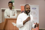 Foto mostra um homem falando no microfone.