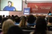 Foto mostra um tel&atilde;o com a imagem de L&aacute;zaro Ramos. Em primeiro plano, h&aacute; v&aacute;rias pessoas sentadas de costas.