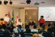 Foto mostra pessoas em um palco de audit&oacute;rio falando para outras pessoas que est&atilde;o sentadas no audit&oacute;rio