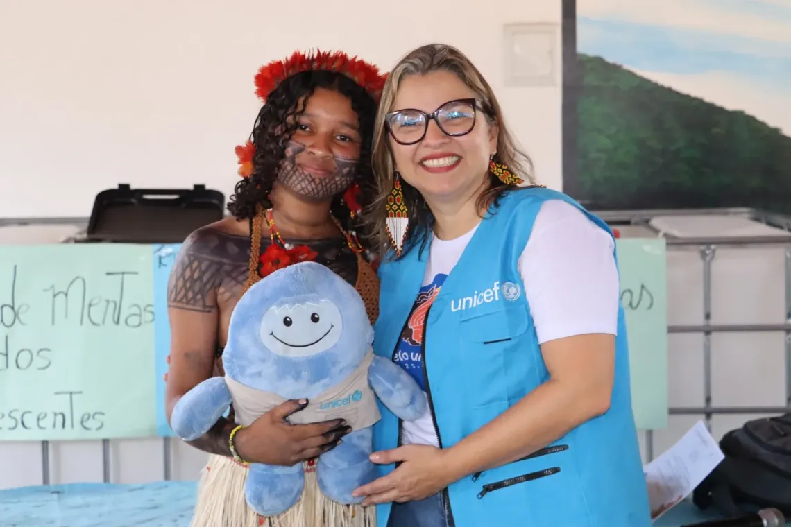 jovem ind&iacute;gena e funcion&aacute;ria vestindo colete do UNICEF seguram boneco de pel&uacute;cia, mascote do UNICEF Unicefito