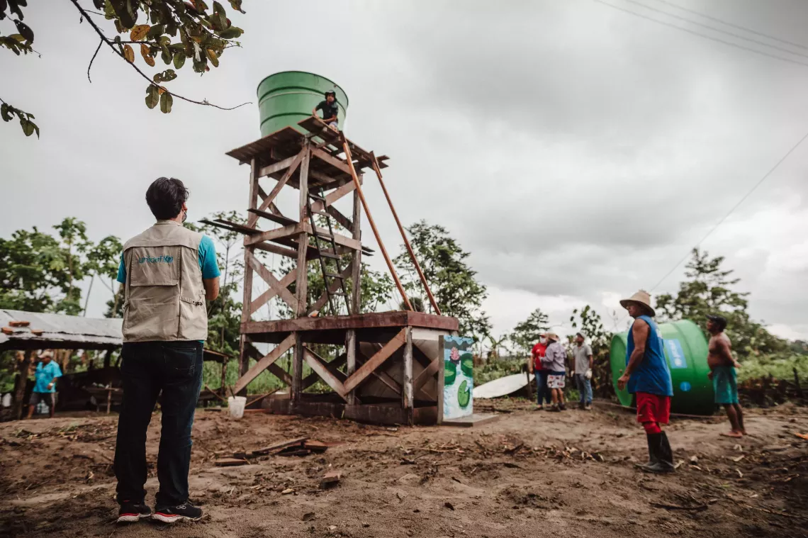 Funcion&aacute;rio do UNICEF uniformizado olha uma caixa d'&aacute;gua acompanhado de outras pessoas. 