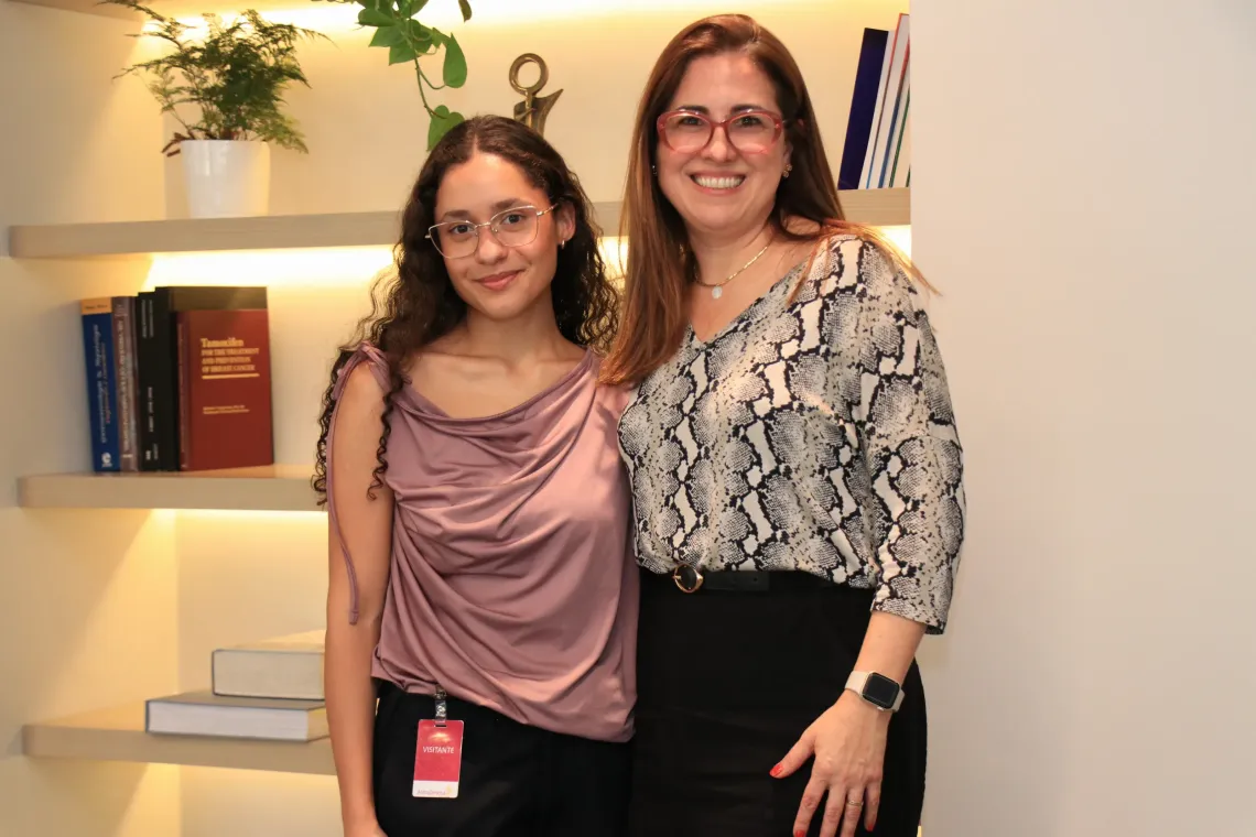 mulher e menina posam para foto em frente a estante de livros