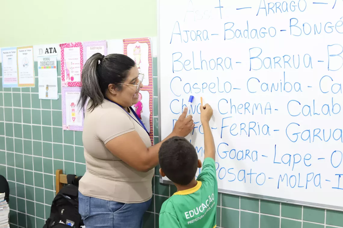 professora ajuda aluno com atividade no quadro branco