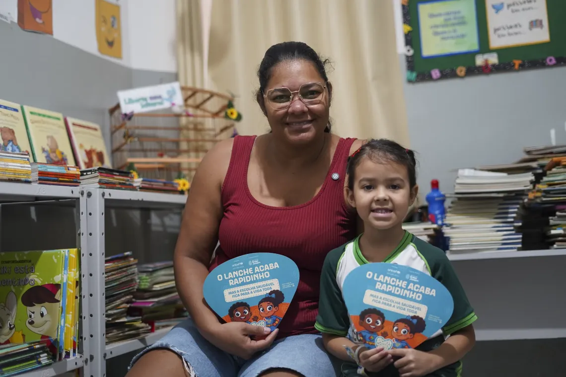 mulher e menina com cartazes do projeto Bora Comer bem, do UNICEF