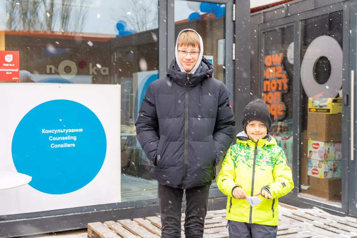 Foto mostra um adolescente e uma crian&ccedil;a em p&eacute; do lado de fora de uma constru&ccedil;&atilde;o de vidro, onde se v&ecirc; um c&iacute;rculo azul. Os dois meninos est&atilde;o usando roupas de frio.