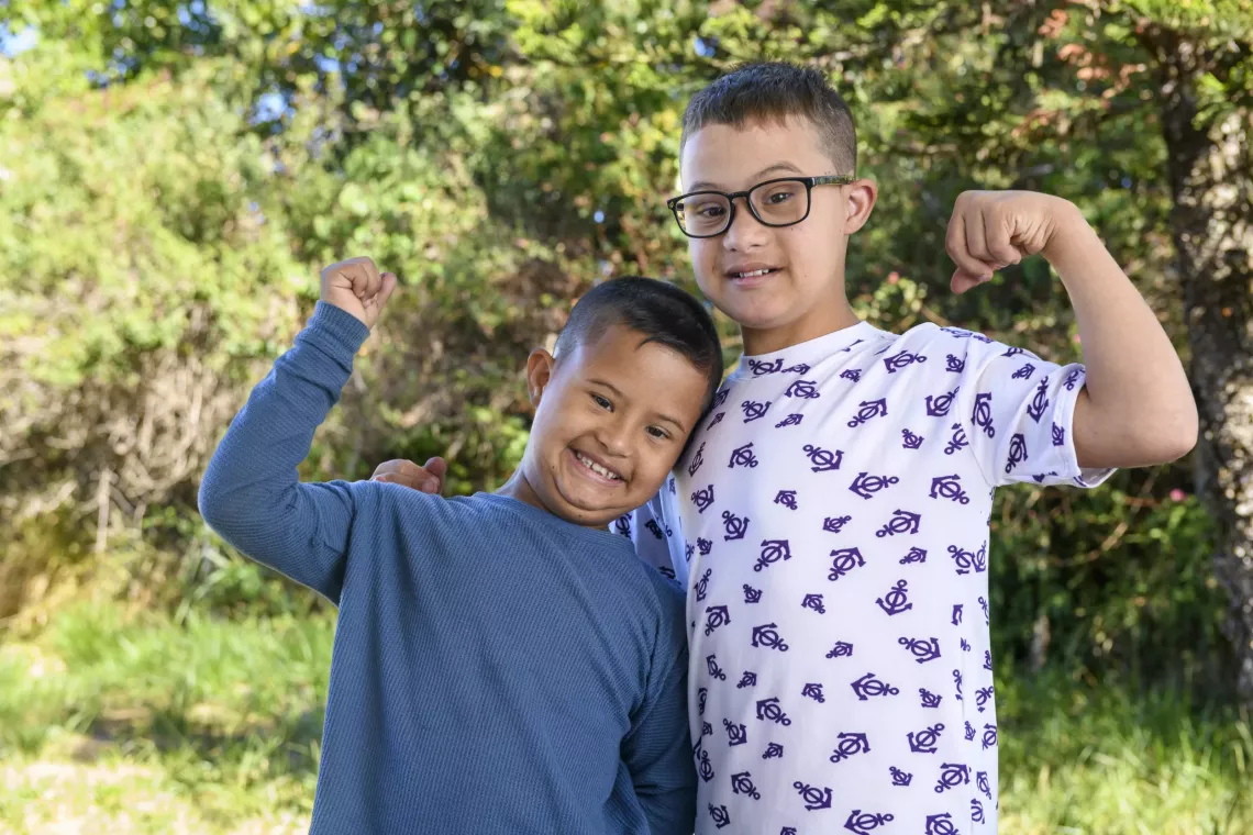 dois meninos se abra&ccedil;am e sorriem para a foto, cada um com um punho fechado 