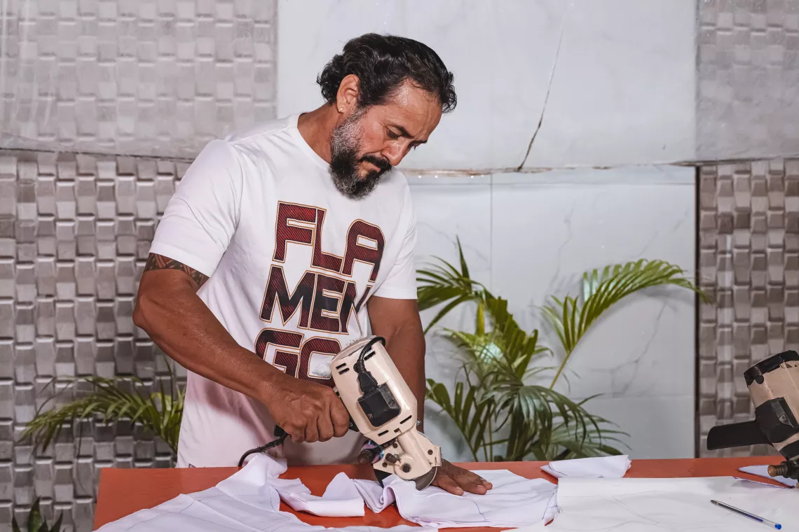 Foto mostra um homem cortando tecido.