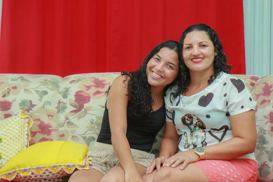 uma adolescente e sua m&atilde;e est&atilde;o sentadas em um sof&aacute;, abra&ccedil;adas e sorrindo