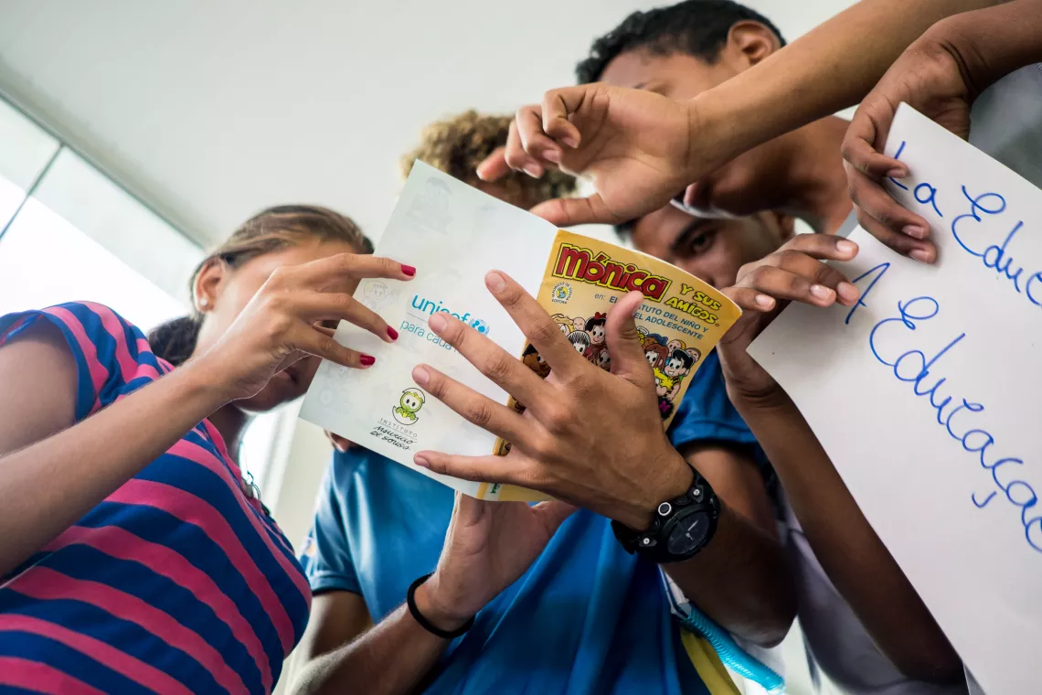 a foto mostra em primeiro plano as m&atilde;os de tr&ecirc;s crian&ccedil;as segurando e apontando para o gibi sobre o Estatuto da Crian&ccedil;a e do Adolescente em espanhol.