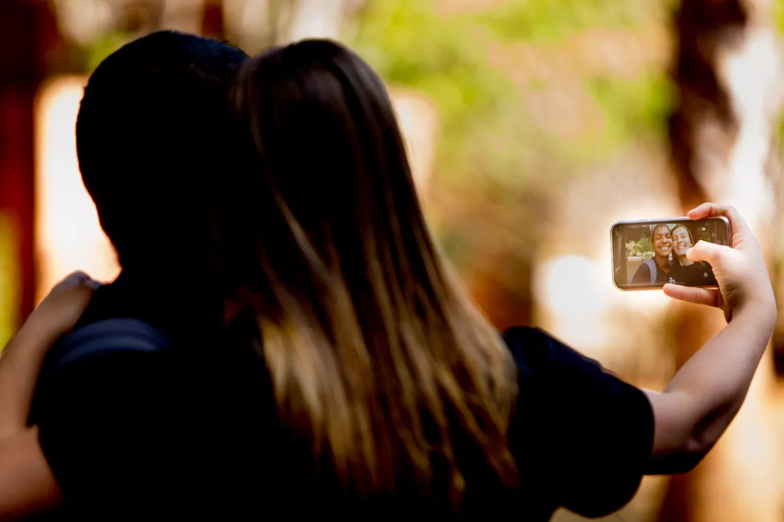 dois adolescentes est&atilde;o de costas para a c&acirc;mera e tiram uma 'selfie' com o celular de um deles