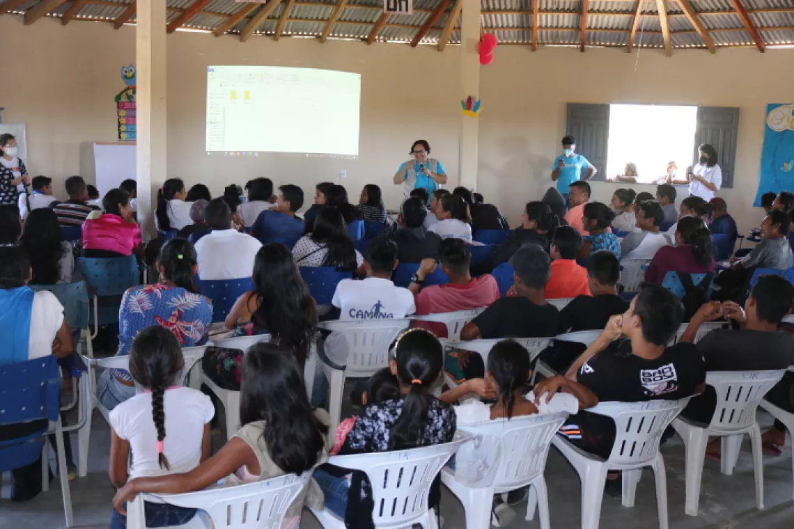 Foto mostra uma sala lotada de pessoas sentadas de costas para a foto. Na frente, h&aacute; uma funcion&aacute;ria do UNICEF em p&eacute;, falando.