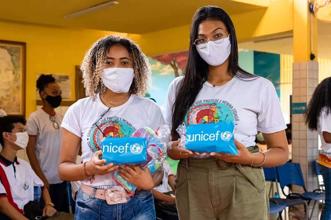 Foto mostra duas jovens segurando um pacote que tem o logo do UNICEF. Elas est&atilde;o usando m&aacute;scara.