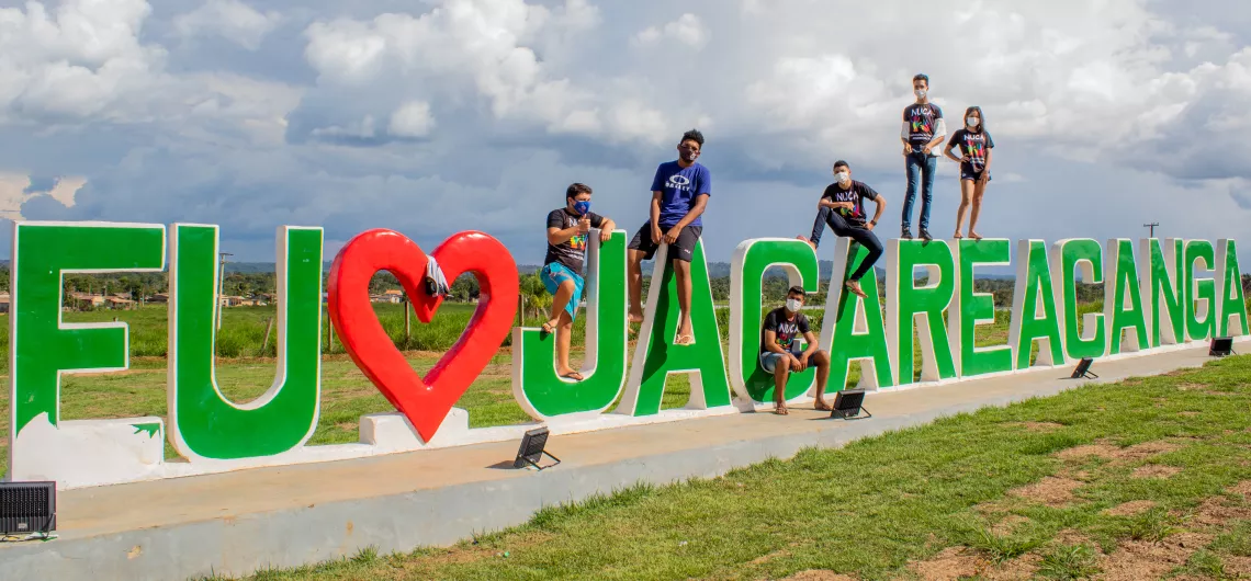 grupo de jovens posa para foto em cima de escultura que diz "eu amo jacareacanga"