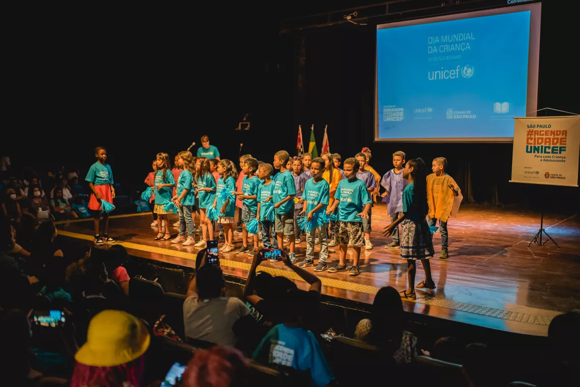 Foto mostra um grupo de meninas e meninos em um palco