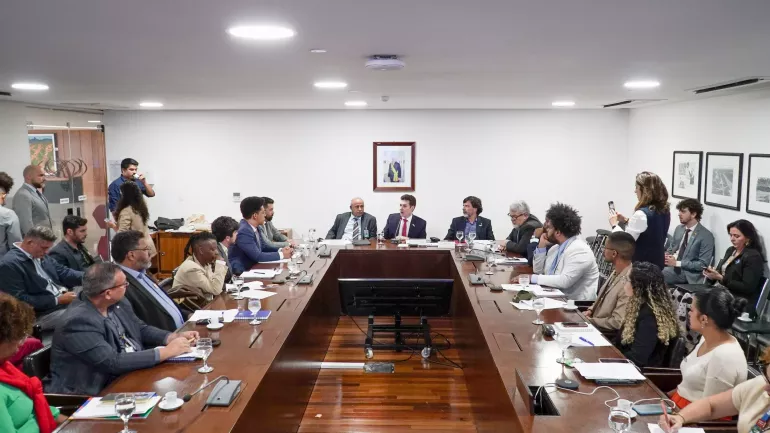 pessoas sentadas em volta de uma mesa em formato de U