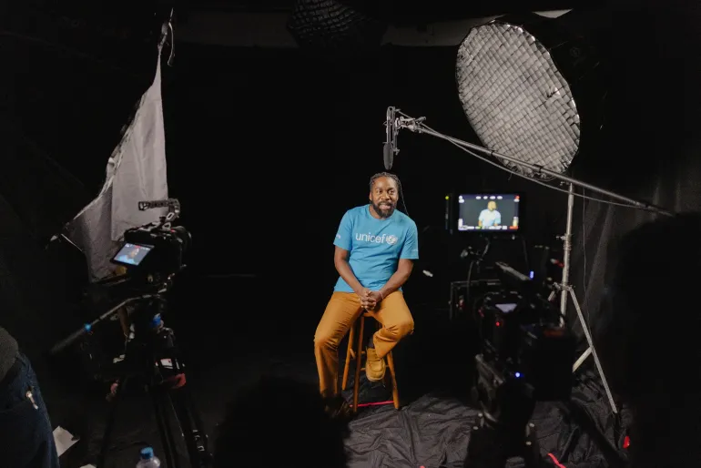 ator negro sentado em banco de est&uacute;dio vestindo camiseta do UNICEF