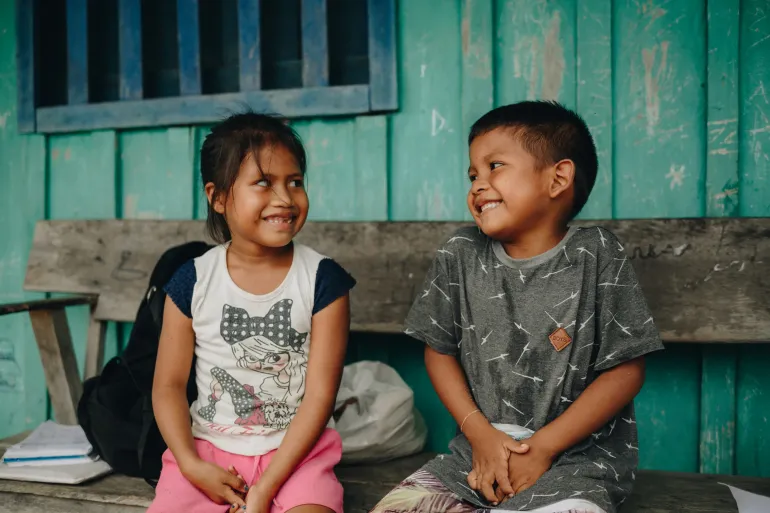 duas crian&ccedil;as sorrindo sentadas em um banco de madeira 