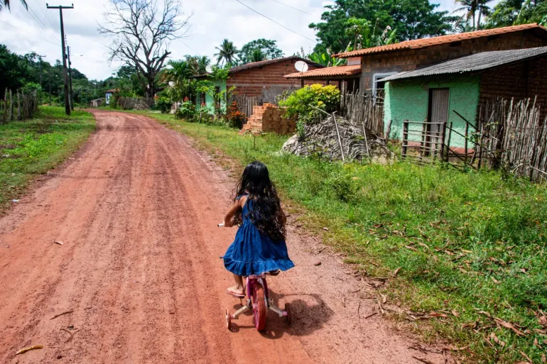 Crian&ccedil;a de costas andando de bicicleta em uma estrada de terra em Bequim&atilde;o