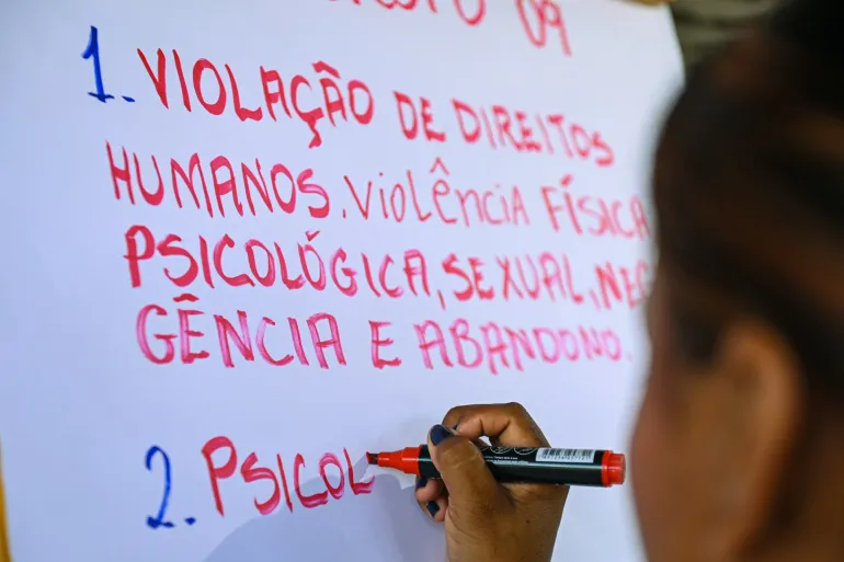 adolescente escreve em papel branco com tinta vermelha e se l&ecirc; um par&aacute;grafo sobre viola&ccedil;&atilde;o de direitos humanos