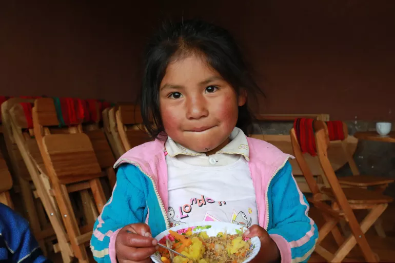 uma menina segura um prato com comida e uma colher. ela est&aacute; olhando para a foto e sorrindo.