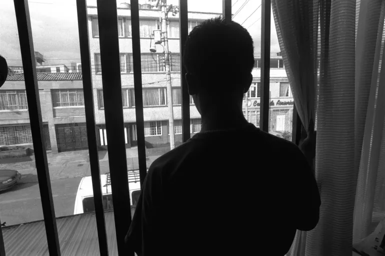 Jovem olha atrav&eacute;s de grades de casa pra rua em uam cidade