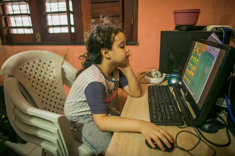 um menino est&aacute; sentado mexendo no computador