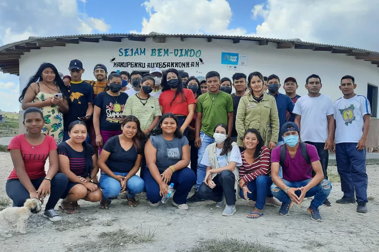Foto mostra um grupo grande de adolescentes e jovens posando para a foto. Eles est&atilde;o ao ar livre, em frente a uma constru&ccedil;&atilde;o.