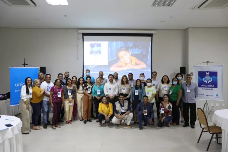 Grupo de pessoas posa para a foto. Atr&aacute;s deles h&aacute; uma proje&ccedil;&atilde;o de power point.