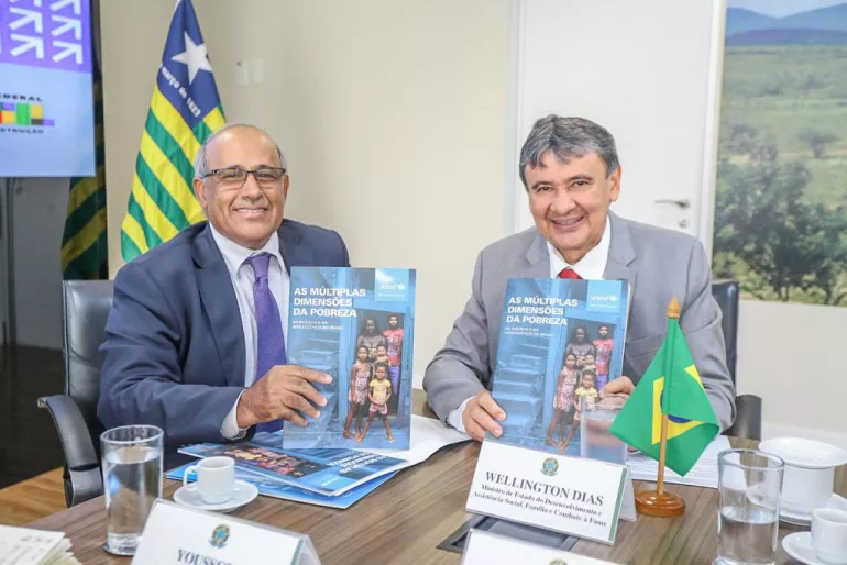 Foto mostra o representante do UNICEF no Brasil e o ministro de Desenvolvimento Social do Brasil sentados a uma mesa de reuni&otilde;es. Eles est&atilde;o segurando uma publica&ccedil;&atilde;o e olhando para a c&acirc;mera e sorrindo.