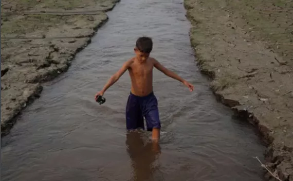 menino caminha em um canal de &aacute;gua