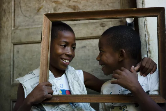 Dois meninos olham um para o outro enquanto sorriem. H&aacute; uma moldura vazia na frente deles.