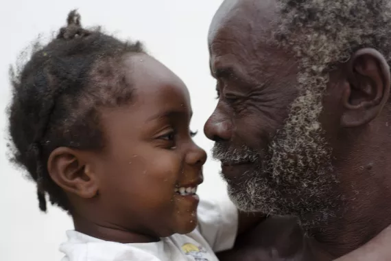 Uma menininha olha para o av&ocirc;. Ela est&aacute; sorrindo.