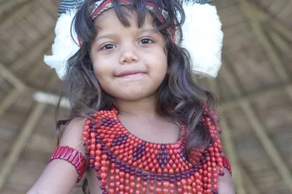 Menina ind&iacute;gena olha para a c&acirc;mera. Ela est&aacute; com uma roupa de mi&ccedil;angas.