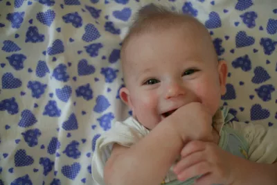 a few months old baby is smiling with hands in his or her mouth