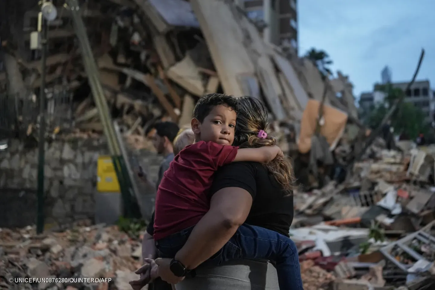 A woman holding a young boy in Caracas, Venezuela, walks past a collapsed building following powerful twin earthquakes on 25 June 2026.