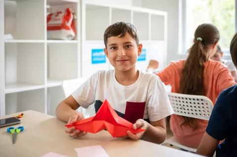A refugee boy holds a paper boat in his hands during the summer workshop in Plovdiv