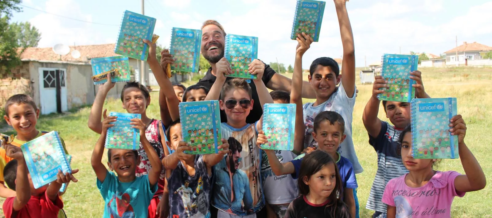 Boys and girls pose with unicef notebooks on the green field.