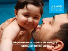 Баща прегръща бебето си и го целува по бузата. Двамата се усмихват и се радват на тази комуникация.