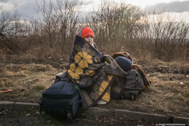 Момиче седи само, завито с одеяло, край път на границата между Украйна и Румъния