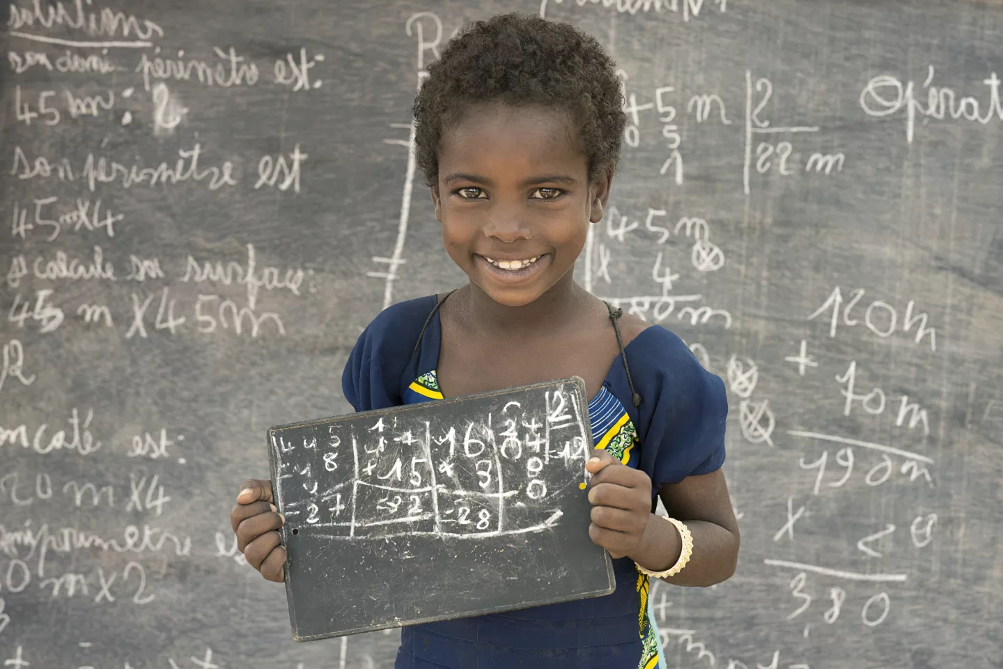 School girl standing in front of the blackboard, holding wooden tablet
