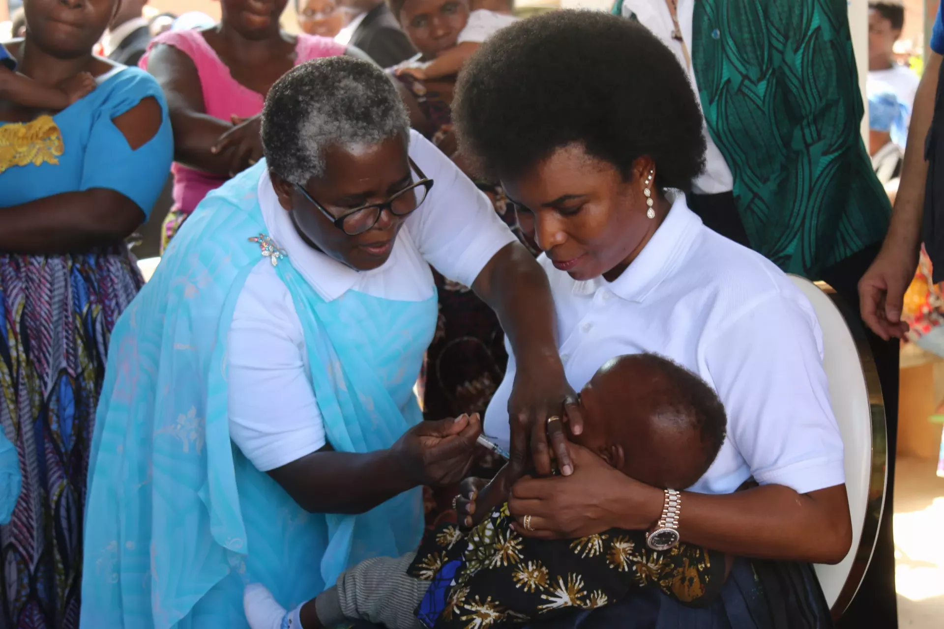 La Premi&egrave;re Dame du Burundi, SE Angeline Ndayishimiye, tenant un enfant pendant que la ministre de la Sant&eacute; lui administre le vaccin antipaludique. 