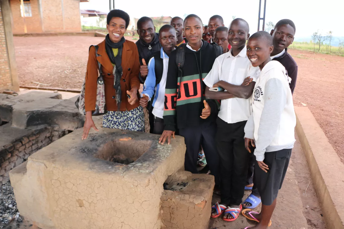 Isidonie Nzeyimana and her students by showing a big improved cookstove made in the High School.