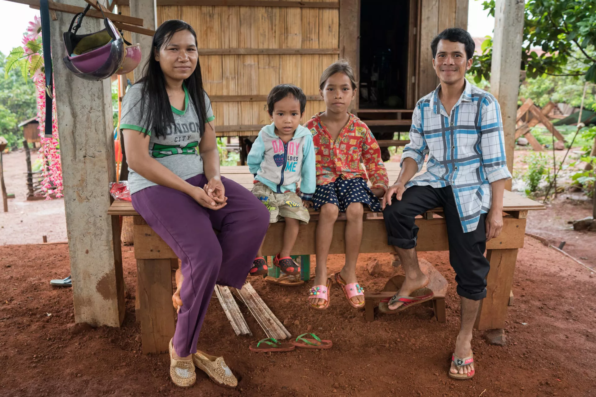 2 year old Yin Ratana, his mother Leav Channy, father Pov Vanny, and sister Sok Rotanaklina pose for a photo in front of their home